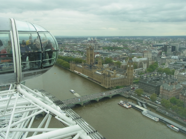 Luftaufnahme des Parlamentsgebäudes in London mit einer Brücke, zahlreichen Gebäuden und einer bewölkten Himmel.