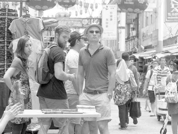 Ein belebter Marktplatz mit Menschen und Ständen auf beiden Seiten und Plakaten in der Mitte.
