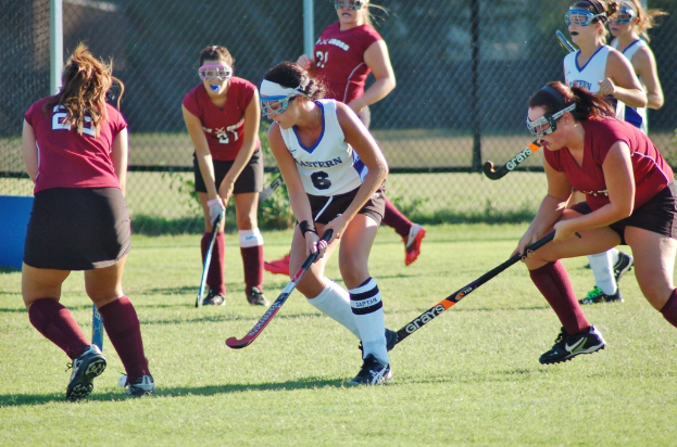 Frauen beim Hockey auf einem Rasenfeld mit einem Netz im Hintergrund.