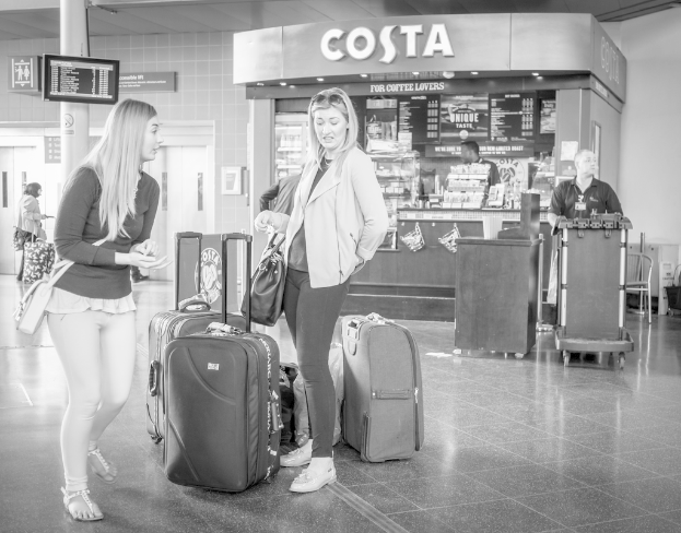 Zwei Frauen mit Gepäck vor einem Café, wahrscheinlich am Flughafen.