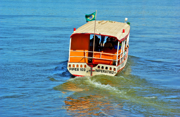 Ein Boot mit Menschen an Bord und eine Flagge mit Text fährt auf dem Wasser.
