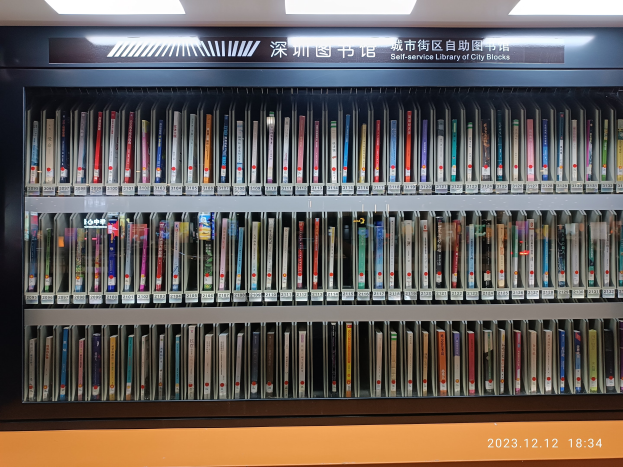 Eine gut beleuchtete Bibliothek mit hohen Bücherregalen voller Bücher, ein Textbrett und ein Wasserzeichen unten, das an eine Selbstbedienungsbibliothek von Stadtblöcken erinnert.