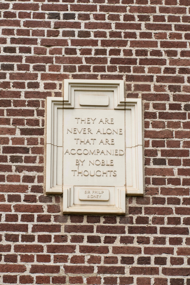 Ein Steinplakette an einer Backsteinwand mit der Inschrift "Sie sind nie allein, die von edlen Gedanken begleitet sind" in fetter Schrift.