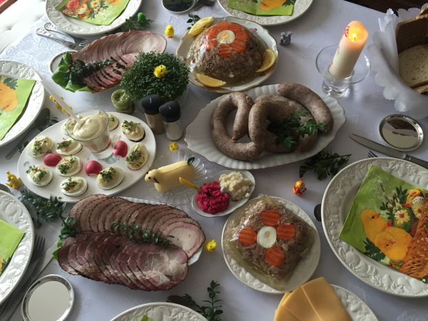 Ein langer Tisch mit verschiedenen Gerichten, Besteck, Gläsern und Kerzen, umgeben von Stühlen, das Bild einer traditionellen deutschen Oster-Mahlzeit.