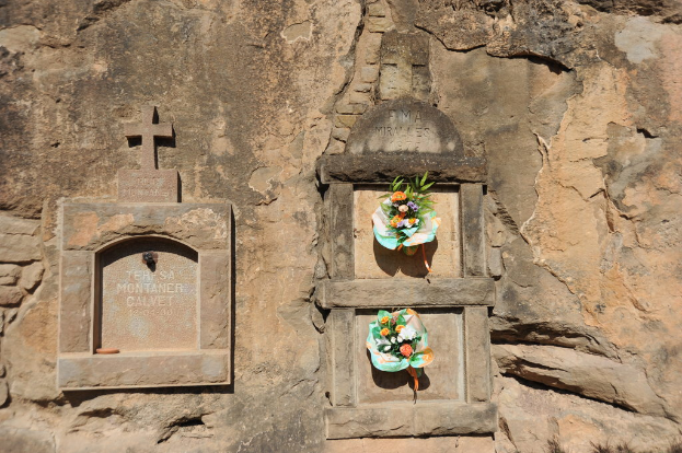 Denkmäler, die in eine Wand gemeißelt sind, mit Blumensträußen davor.