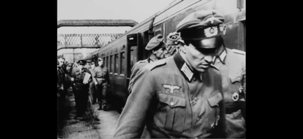 Eine Gruppe von Männern in Militäruniformen steht neben einem Zug mit einer Brücke und Himmel im Hintergrund und sieht besorgt aus auf diesem Schwarz-Weiß-Bild.