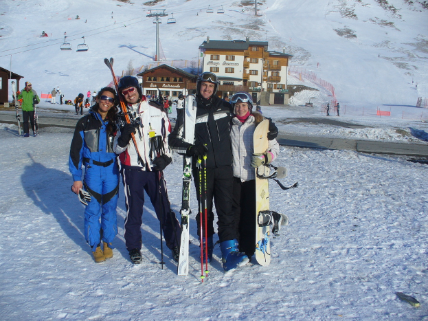 Vier Personen posieren für ein Foto mit Skatpad und Werkzeugen, mit Gebäuden und anderen Menschen im Hintergrund, vor einer schneebedeckten und vereisten Berglandschaft.