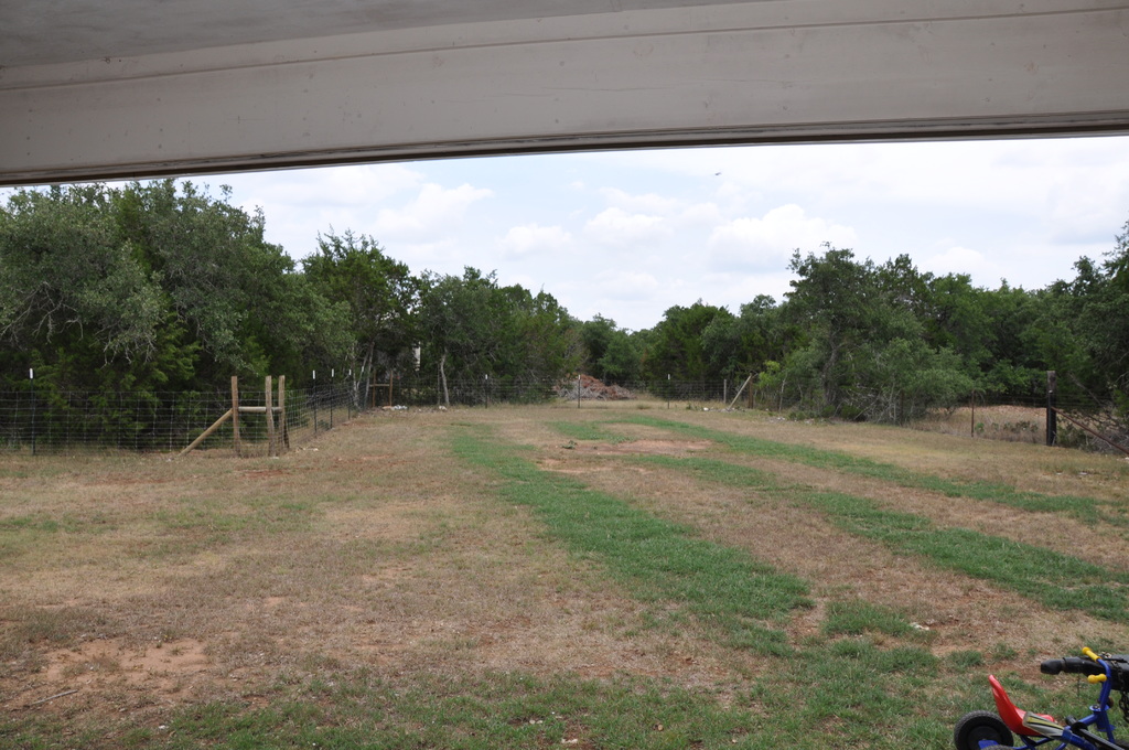 Eine offene grüne Wiese, die von einem Zaun mit Bäumen im Hintergrund umgeben ist und ein Fahrzeug auf der rechten Seite geparkt ist.