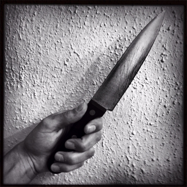 Ein Schwarz-Weiß-Bild einer Hand, die ein Messer hält, mit einer Wand im Hintergrund.