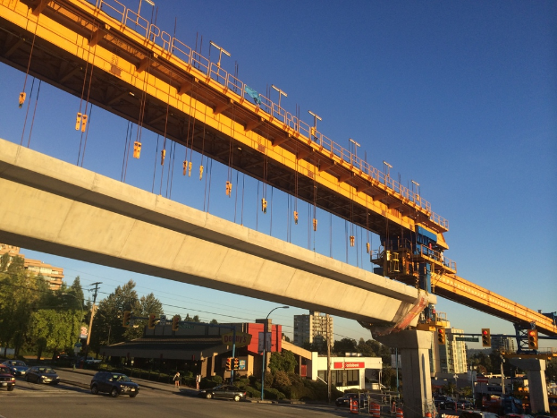 Eine Baustelle in der City mit Fahrzeugen und Gebäuden links, unter einem blauen Himmel.