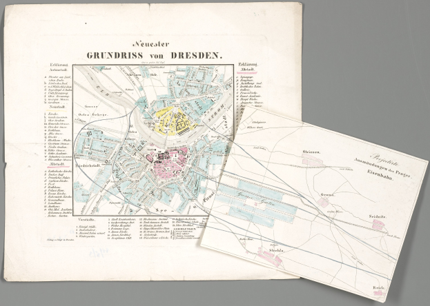 Ein alter Stadtplan von Dresden, Deutschland, der Straßen, Gebäude und Sehenswürdigkeiten zeigt, mit zwei Papieren im Vordergrund und einem grauen Hintergrund.