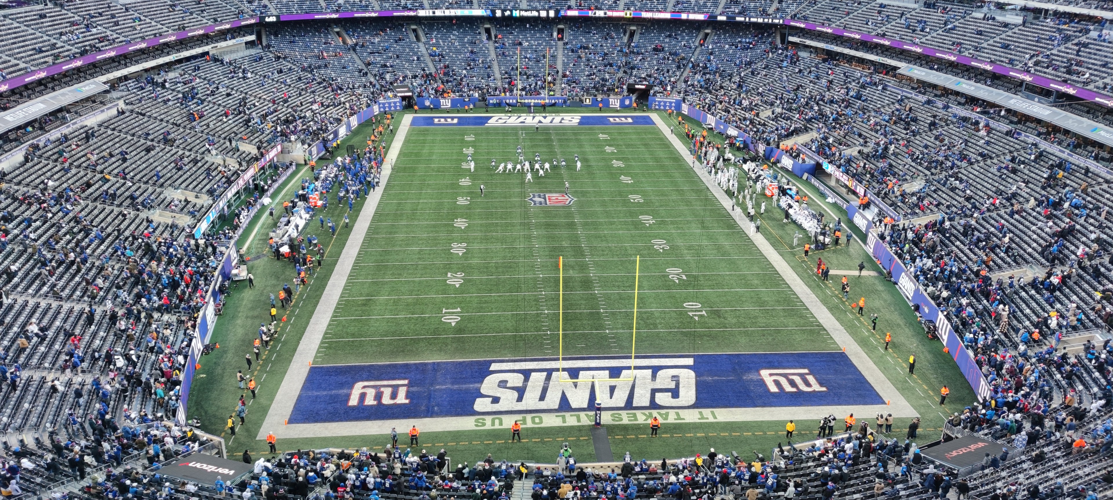 Ein voller Fußballstadion mit Spielern auf dem Feld, Torpfosten und Zuschauern auf den Sitzplätzen unter einer lebendigen Atmosphäre.