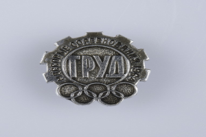 Ein silbern glänzender Abzeichen mit der Aufschrift 'Olympische Spiele' vor einem weißen Hintergrund.