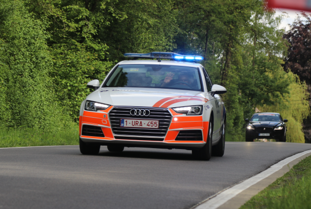 Ein Audi A4 Polizeiwagen fährt auf einer Straße mit Grasrändern, flankiert von einem Wald, mit zwei Insassen, unter einem klaren blauen Himmel.