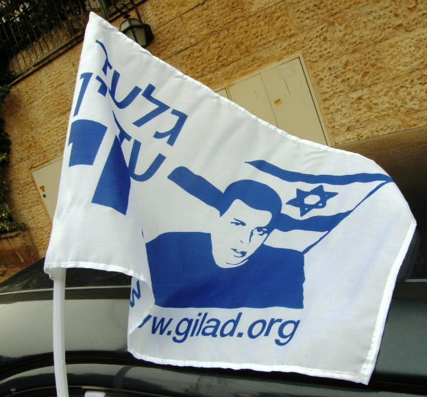 Ein Fahrzeug steht auf einer Straße in der Nähe eines Gebäudes mit einer Flagge, einem Zaun und einer Straßenlaterne.