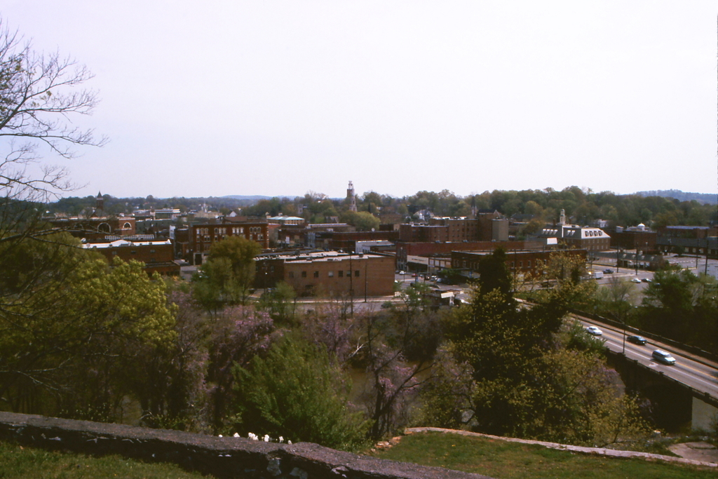 Eine Stadtansicht mit Geb"uden, B"umen, Masten, Stra\ss en, Fahrzeugen und Himmel.