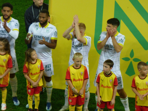 Eine Gruppe von Fußballspielern in Uniformen klatscht auf einem Ligue-1-Feld in celebration.