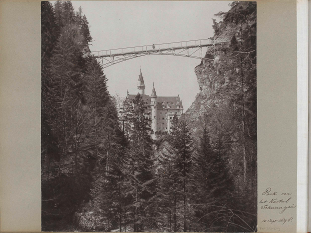 Schwarzes und weißes Foto der Neuschwansteinburg in Deutschland mit einer Brücke im Vordergrund, umgeben von Bäumen und Text auf der rechten Seite.