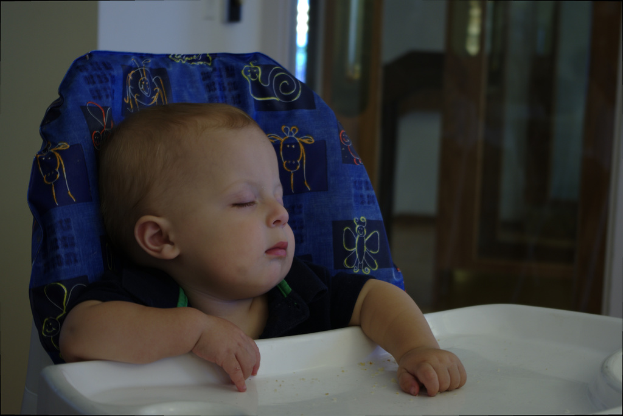 Ein Baby sitzt in einem Stuhl vor einem Tisch mit einer Tür in der Mitte des Bildes.