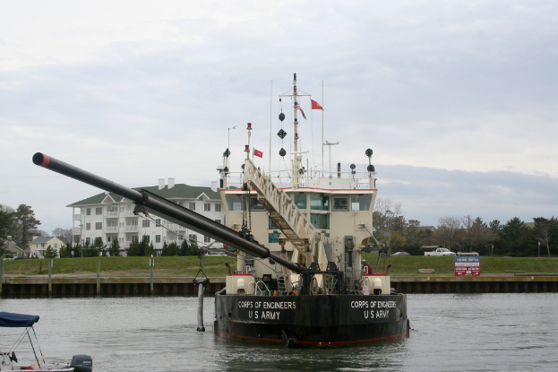 Ein Schiff segelt auf dem Wasser, mit Bäumen, Fahrzeugen, Gebäuden und Pfählen am Ufer und einem Boot in der unteren linken Ecke, mit dem Himmel im Hintergrund.