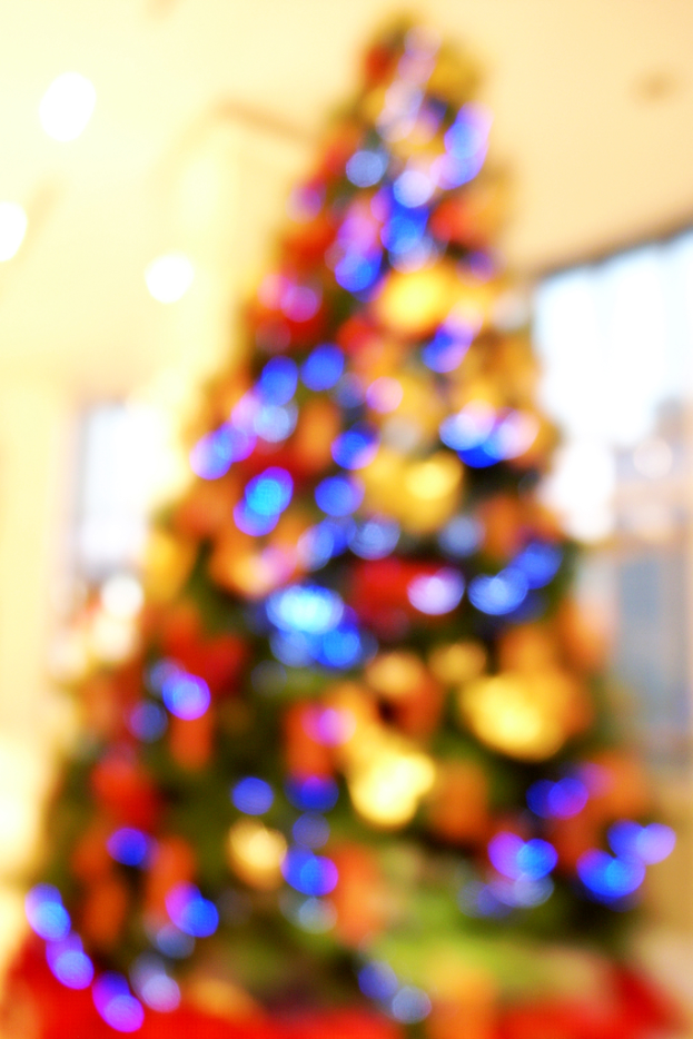 Unscharfe Innenaufnahme mit einem Weihnachtsbaum in der Mitte, der mit Lichtern und Schmuck verziert ist.