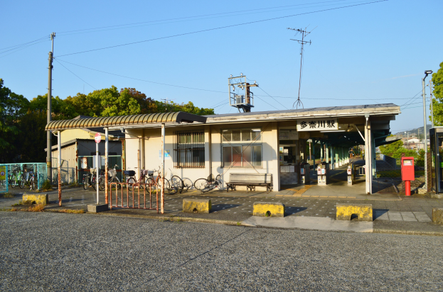 Ein Bahnhof mit Fahrrädern vorne, einer Straße unten und Häusern, Bäumen, Polen, Drähten und einem klaren blauen Himmel im Hintergrund.