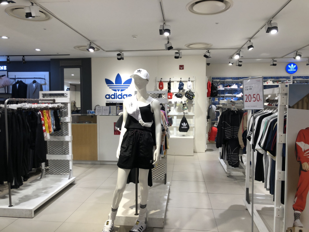 Innenansicht eines adidas-Geschäfts in Singapur mit Schaufensterpuppen, Kleiderständern, einem Textbrett auf der rechten Seite und Deckenlampen.