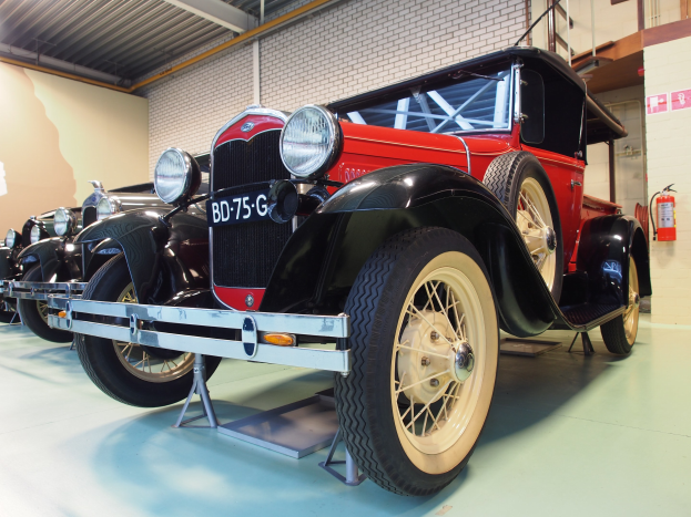 Eine Reihe von Oldtimern aus den 1930er Jahren in einem Museum ausgestellt, mit einem Feuerlöscher auf der rechten Seite und Deckenlampen darüber.