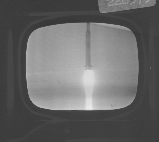 Schwarzes und weißes Foto eines Fernseherbildschirms mit einem durch das Fenster sichtbaren Raketenstart, mit Text oben.