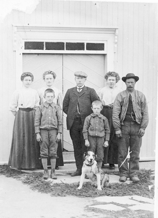 Schwarzes und weißes Foto einer Familie mit einem Hund, die vor einem Haus posieren