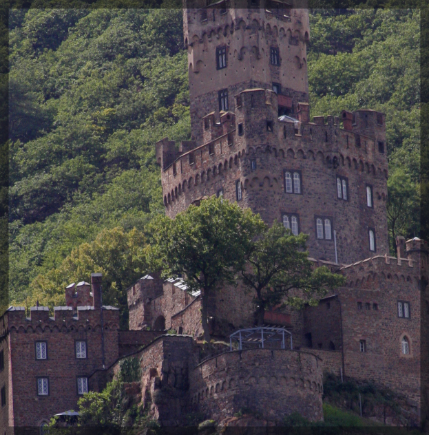 Ein Schloss mit zahlreichen Fenstern im Vordergrund, umgeben von Bäumen im Hintergrund.