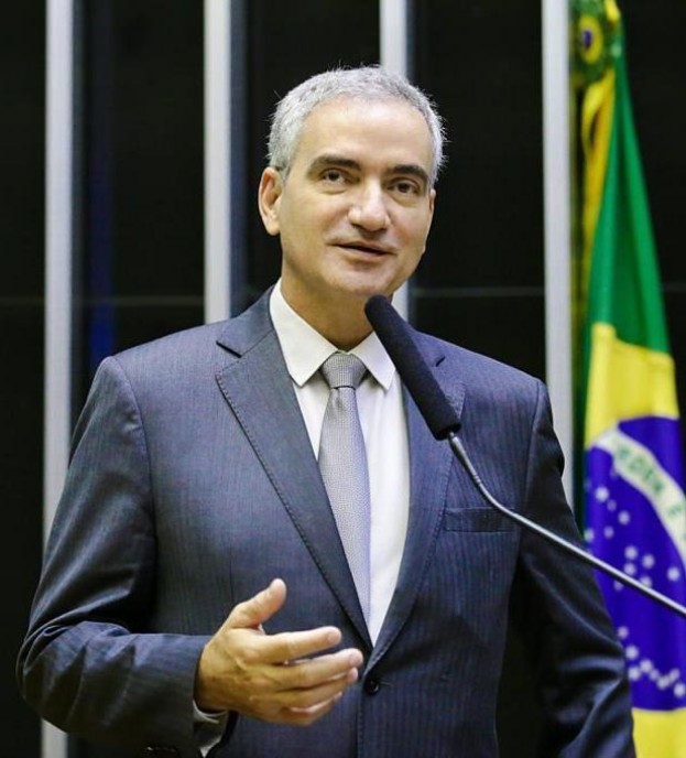 Ein Mann im Anzug und mit Krawatte spricht an einem Rednerpult mit einem Mikrofon, im Hintergrund ist eine brasilianische Flagge zu sehen.