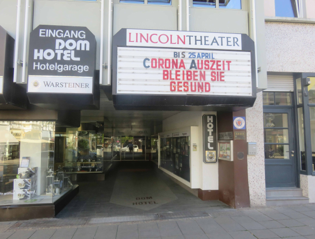Das Lincoln Theater in Berlin, Deutschland, mit Glasfenstern und -türen und einer Tafel mit Text, sowie einem belebten Innenstadtbild.