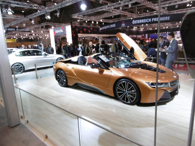 Ein schwarzer BMW i8 Roadster mit glänzender Lackierung und Chromakzenten auf der Frankfurter Motor Show umgeben von formell gekleideten Besuchern.