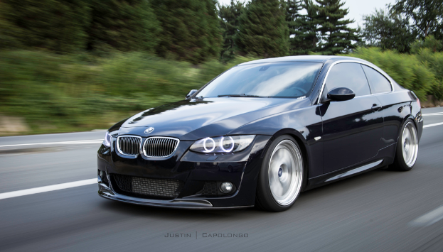 Ein schwarzer BMW fährt auf einer Straße mit Bäumen im Hintergrund.