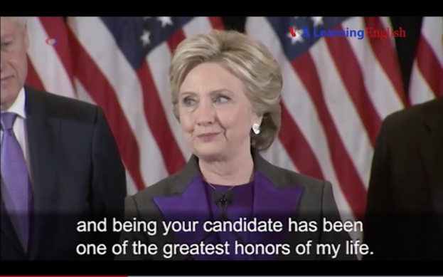 Hillary Clinton und Joe Biden stehen Seite an Seite, beide tragen schwarze Blazer, weiße Hemden und lila Krawatten, mit einer Flagge im Hintergrund und einem Zitat von Hillary Clinton unten.