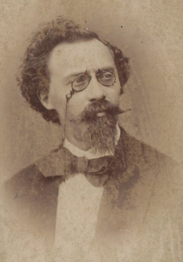 Alte Schwarz-Weiß-Fotografie eines bärtigen Mannes in Anzug und Krawatte mit ernstem Gesichtsausdruck, der eine Brille trägt und einen gepflegten Bart hat.