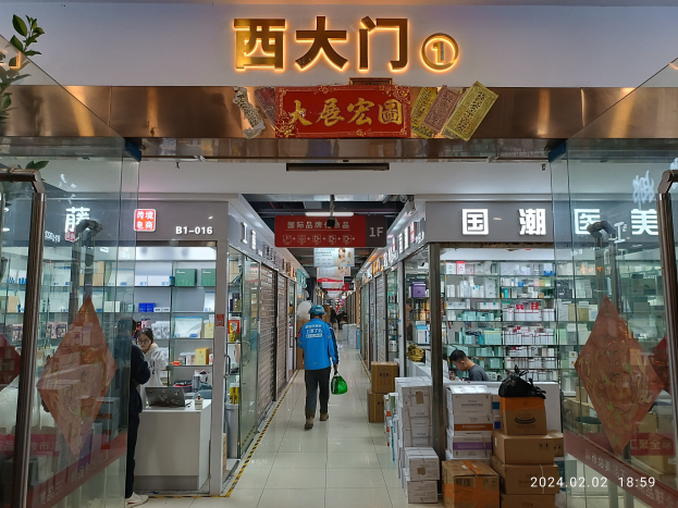 Innenansicht einer chinesischen Apotheke mit Glaswänden, Regalen voller Artikel, verstreuten Kartons, einer Pflanze links und einem Schild oben, das auf eine chinesische Drogerie hinweist.