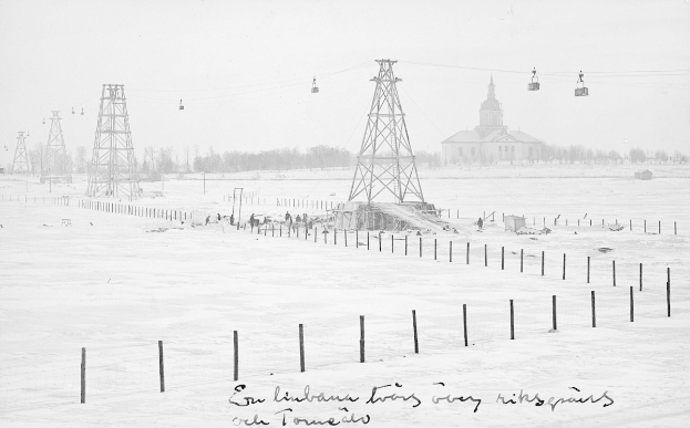 Schwarze und weiße Fotografie eines Skilifts in einem verschneiten Feld mit Stützpfählen, Überseilbahn, Bäumen und einem Gebäude im Hintergrund, mit Text unten.