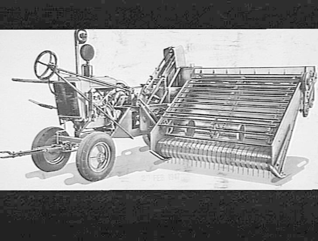 Schwarzes und weißes Foto eines Traktors mit einem Mähdrescher, das ein großes Vorderrad und ein kleineres Hinterrad zeigt.