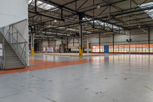 Ein großes industrielles Lagerhaus mit zahlreichen Fenstern, Metallpfosten, einer Treppe mit Geländer, einer Texttafel, Deckenleuchten und zusätzlichen Pfosten.