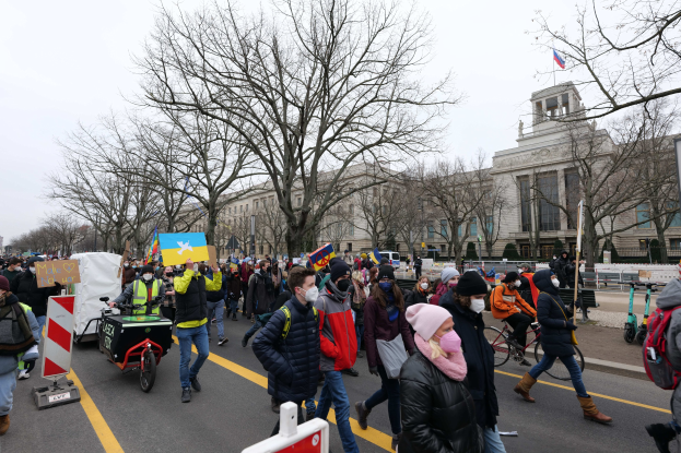 Eine große Gruppe von Menschen nimmt an einer Protestmarsch in Washington, D.C. am 21. Januar 2020 teil, geht eine Straße entlang mit Plakaten, Bannern und Fahrrádern, vor einem Gebäude mit Schildern, Bäumen und einem klaren blauen Himmel.