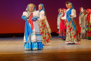 Eine Gruppe von Menschen in farbenfrohen, detaillierten traditionellen ukrainischen Kostümen lächelt fröhlich auf einer Bühne.