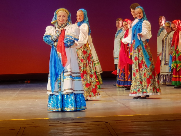 Eine Gruppe von Menschen in farbenfrohen, detaillierten traditionellen ukrainischen Kostümen lächelt fröhlich auf einer Bühne.