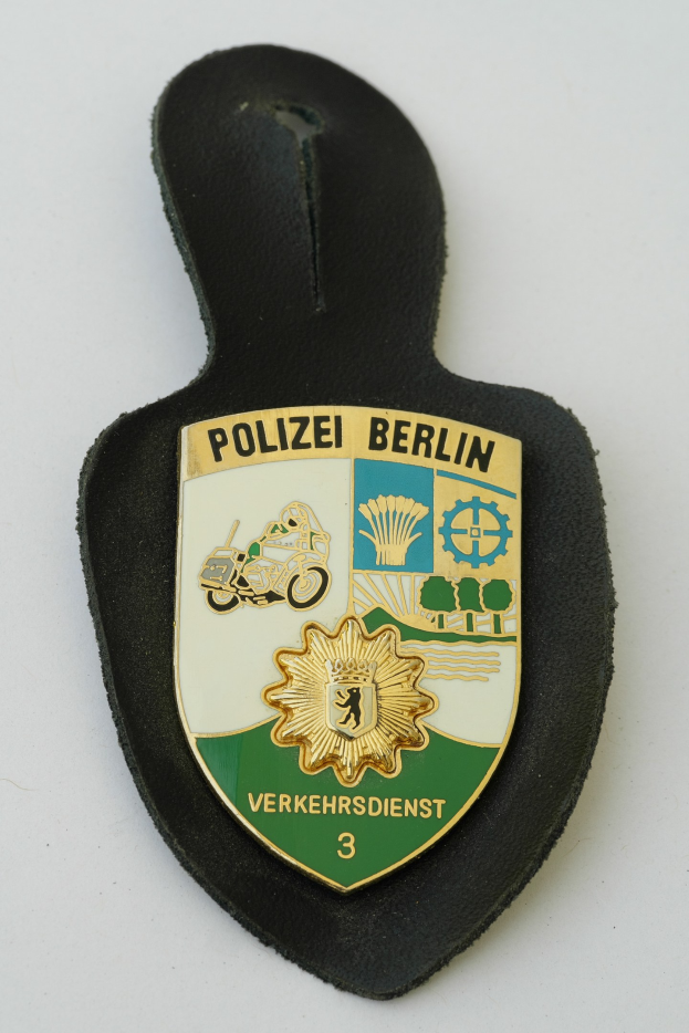 Ein schildförmiges Polizeibadgebnis mit "Polizei Berlin" in schwarzer fetter Schrift, das ein weißes Stern auf einem blauen Hintergrund und einen weißen Rand hat und auf einer Oberfläche ruht.