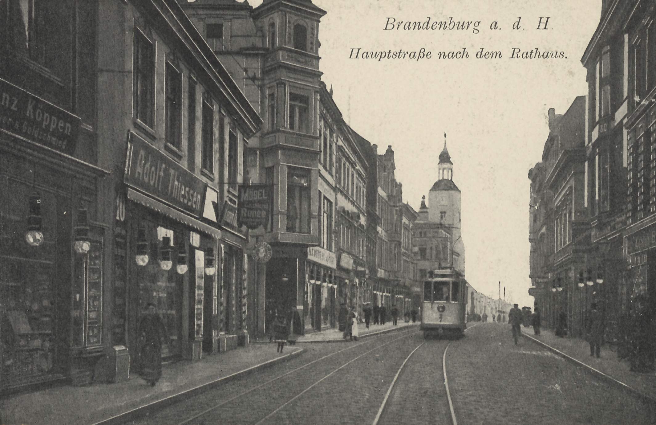 Ein altes Schwarz-Weiß-Foto einer Straßenkreuzung in Brandenburg, Deutschland, mit einer Straßenbahn auf den Schienen, Menschen auf dem Gehweg, Gebäuden mit Fenstern, Schildern und Straßenlaternen unter einem bewölkten Himmel.