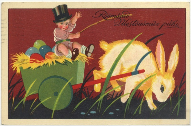 Alte Postkarte mit einem Baby in einem Zylinder, das einen mit bunten Ostereiern gefüllten Handkarren schiebt, begleitet von einem Hasen, mit handgeschriebenen Ostergrü├čen.