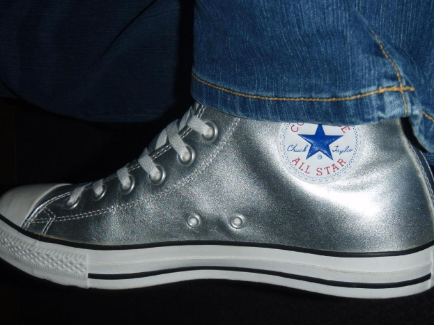 Ein Schuh mit Text und Schnürsenkeln, mit dem Rand einer Jeans in der oberen rechten Ecke, vor einem dunklen Hintergrund.