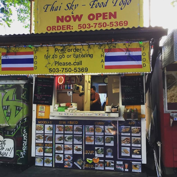 Läden, Getränkedosen, Speisekarten, eine Uhr, Gewürze in Plastikbehältern, Gewürze, Werbetafeln, Namensschilder und Himmel.