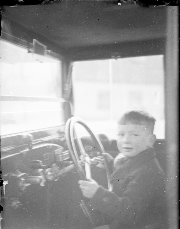 Ein junger Junge in Schwarz-Weiß sitzt im Fahrersitz eines Autos und hält das Lenkrad fest